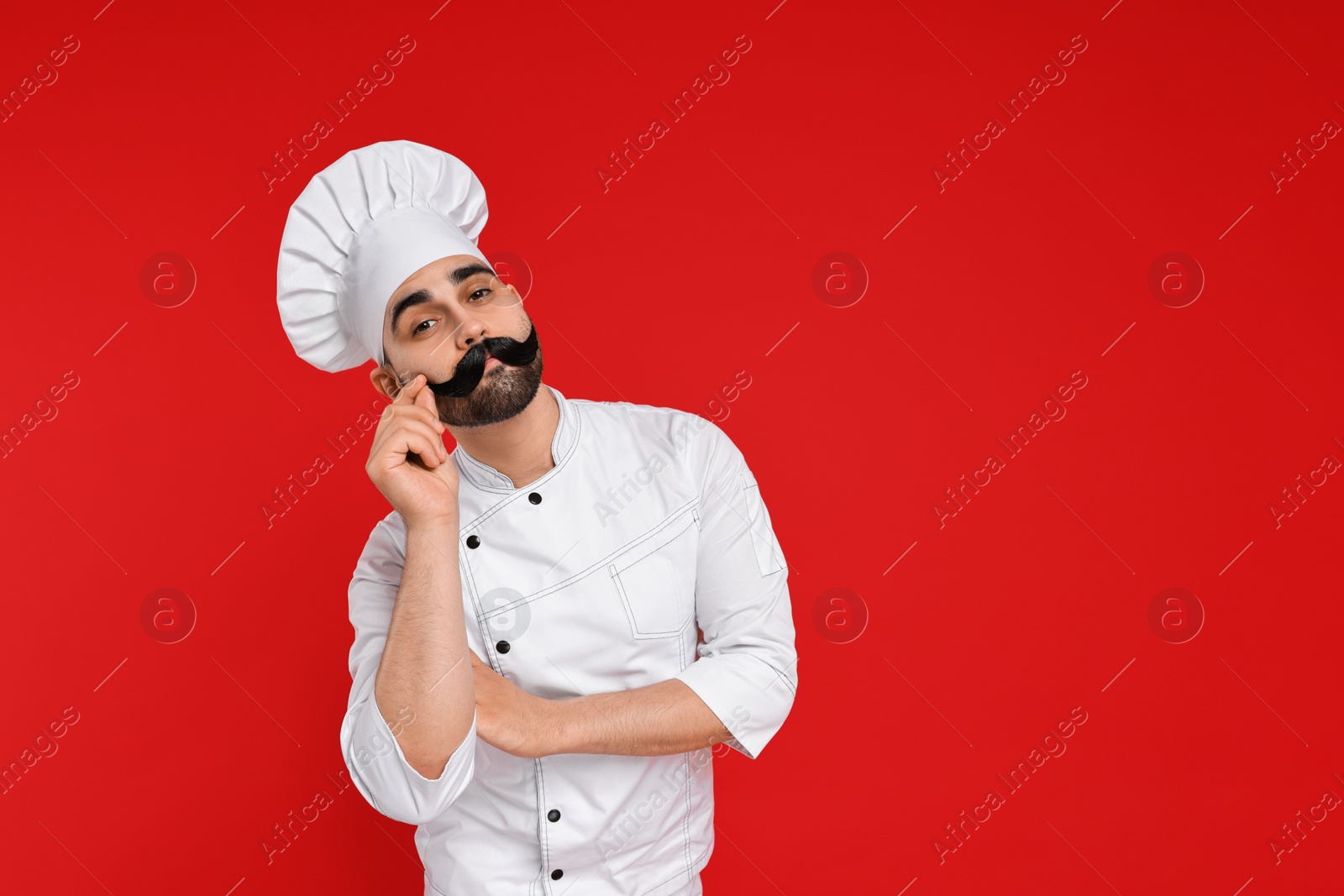 Photo of Professional chef with funny artificial moustache on red background. Space for text
