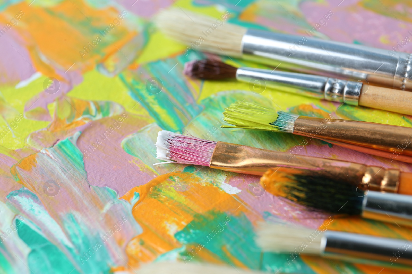 Photo of Set of different brushes on abstract colorful paint, closeup