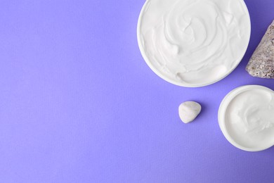 Photo of Jars of cream and stones on violet background, flat lay. Space for text