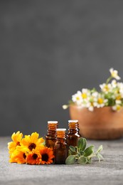 Photo of Bottles with essential oils, flowers and sage on grey textured table. Space for text