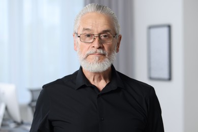 Portrait of handsome senior man in black shirt and eyeglasses at home