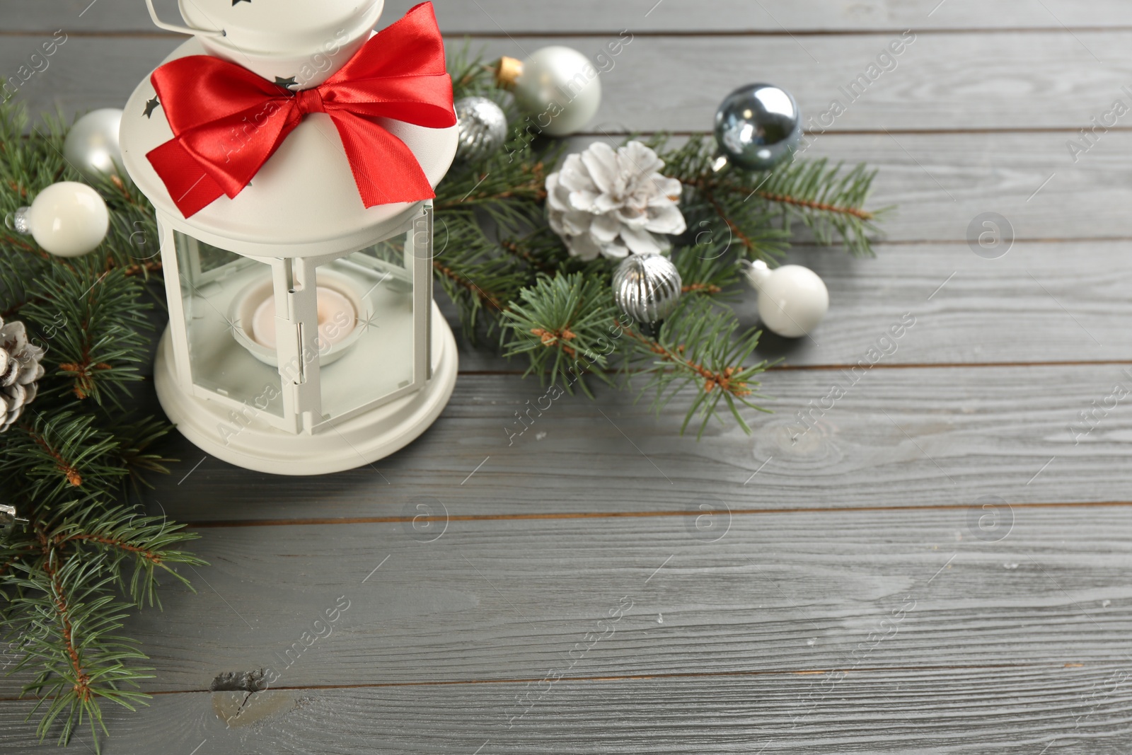 Photo of Christmas lantern with burning candle and festive decor on grey wooden table. Space for text