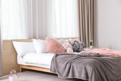 Comfortable bed with pillows and plaid in modern room interior