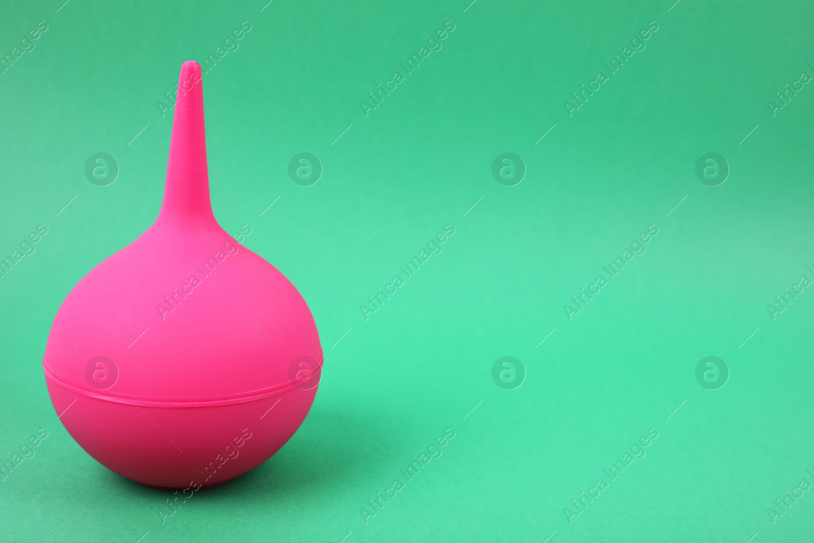 Photo of Pink enema on green background, space for text. Medical treatment