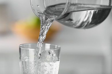 Pouring water from jug into glass on blurred background, closeup