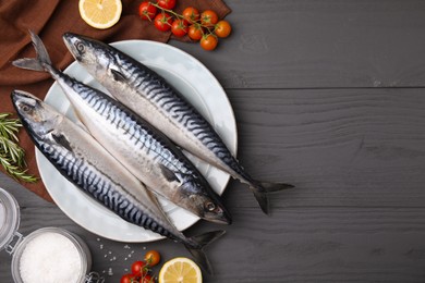 Photo of Raw mackerel, tomatoes and lemons on black wooden table, flat lay. Space for text