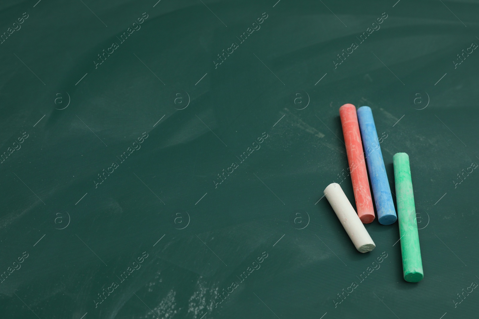 Photo of Colorful chalks on green board, above view. Space for text