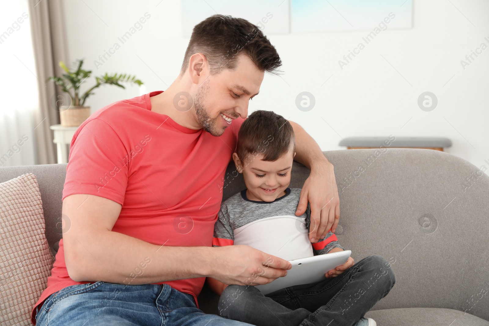 Photo of Boy and his father with tablet sitting on sofa at home. Family time