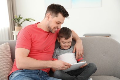 Boy and his father with tablet sitting on sofa at home. Family time