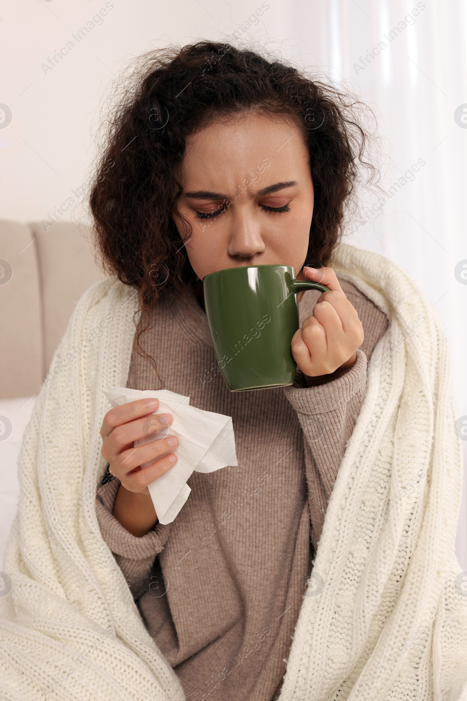 Photo of Sick African American woman with tissue and cup of drink in bed at home