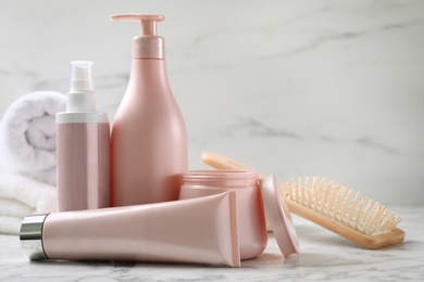 Photo of Set of hair cosmetic products and brush on white marble table