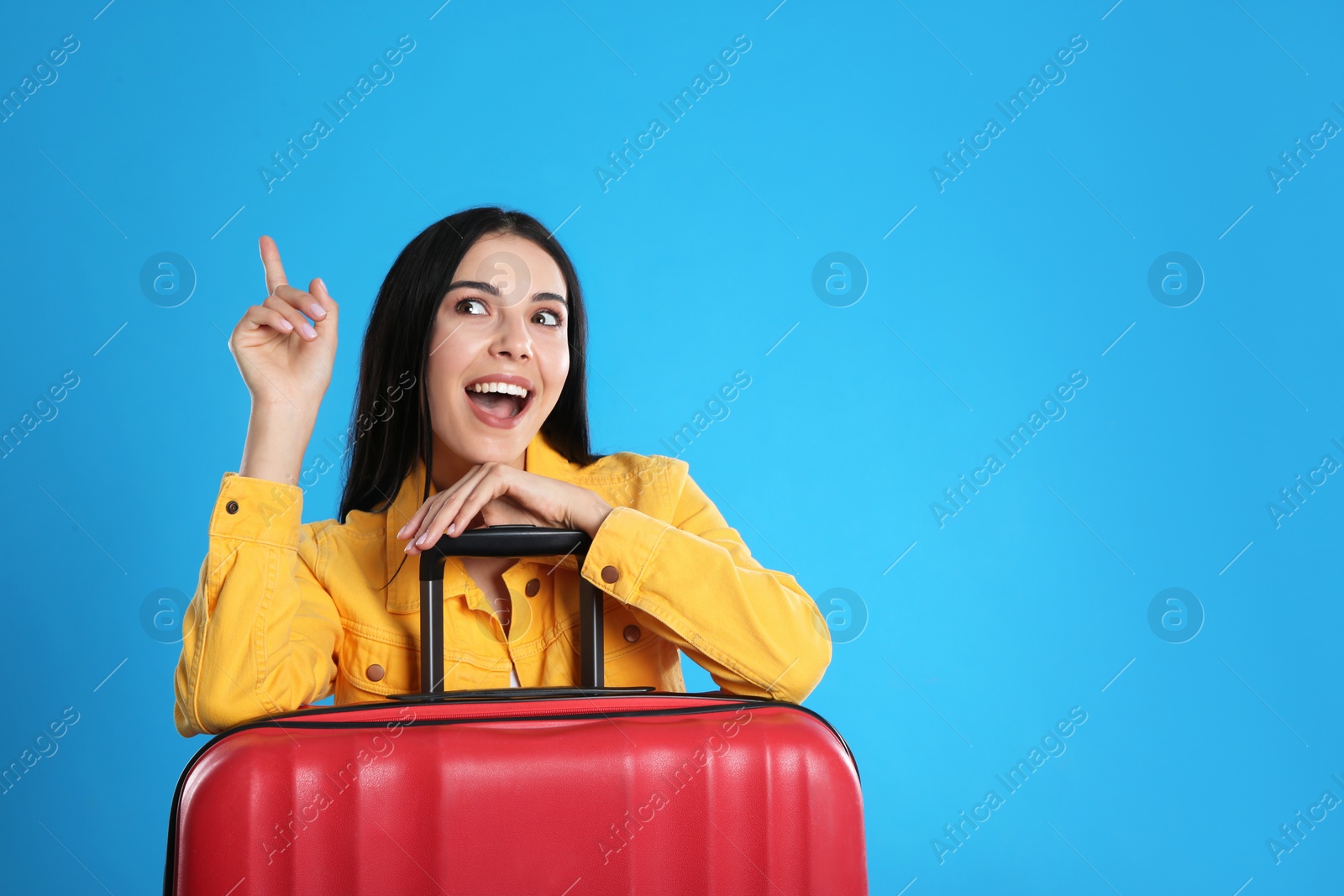 Photo of Beautiful excited woman with suitcase for summer trip on blue background, space for text. Vacation travel