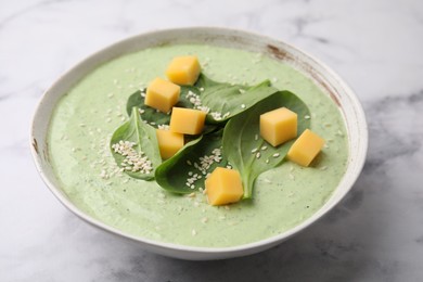 Delicious spinach cream soup with cheese and sesame seeds in bowl on white marble table