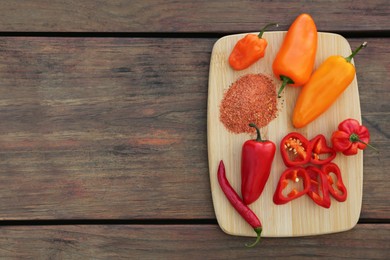 Photo of Many different peppers and spoon with spice on wooden table, top view. Space for text