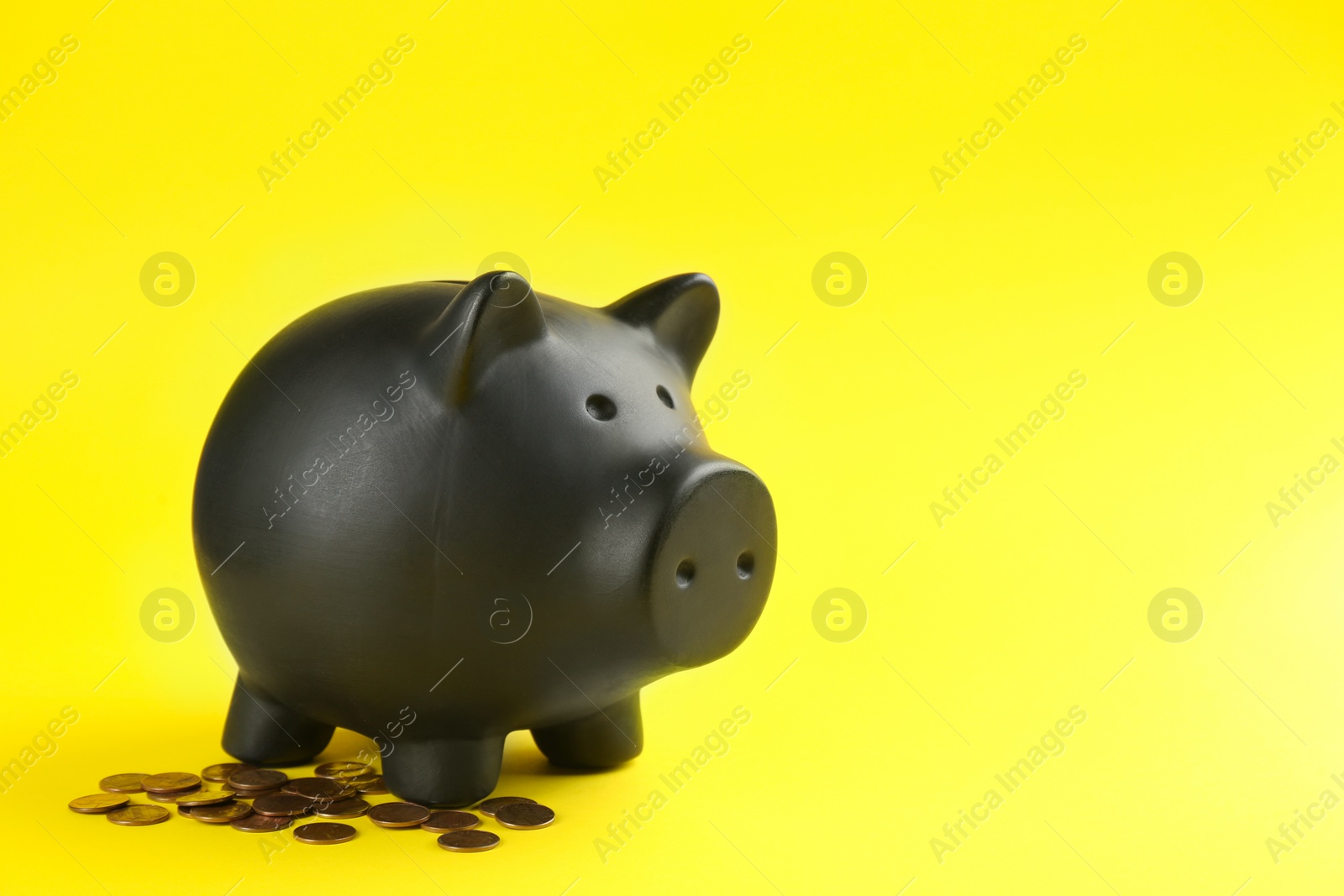 Photo of Black piggy bank and coins on yellow background. Space for text