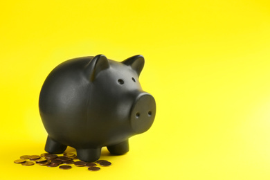 Black piggy bank and coins on yellow background. Space for text