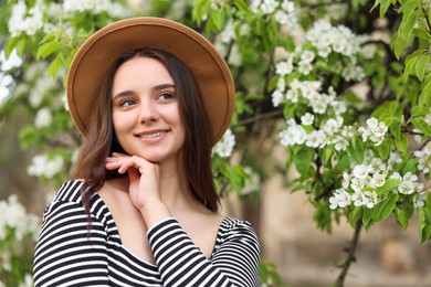 Photo of Beautiful woman in hat near blossoming tree on spring day