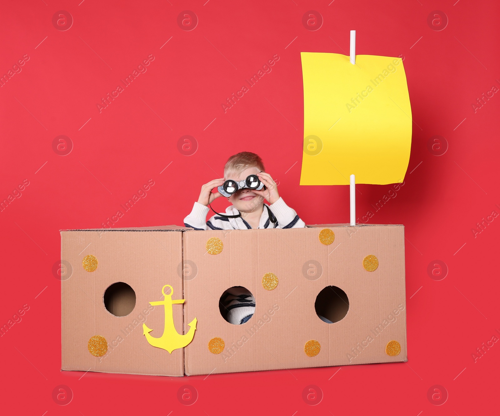 Photo of Little child playing with ship made of cardboard box on red background