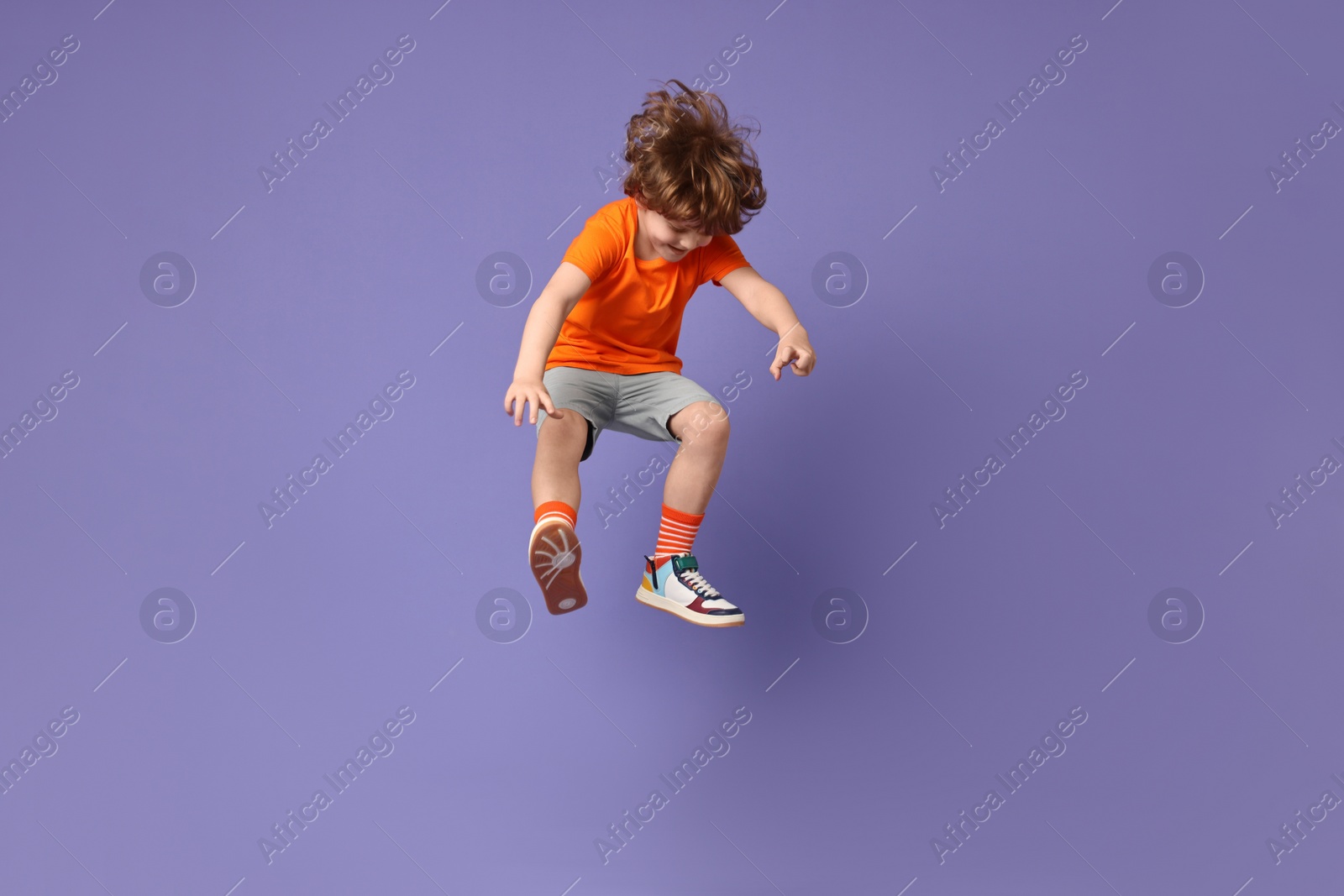 Photo of Happy little boy dancing on violet background