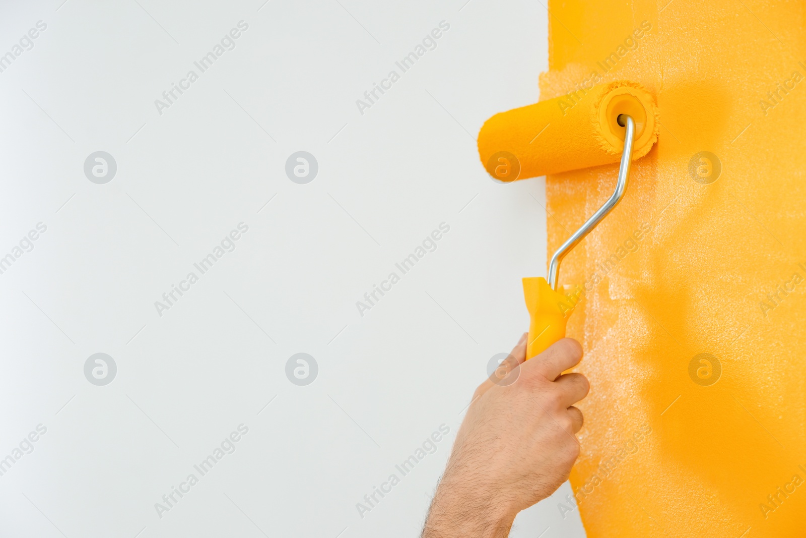 Photo of Man painting white wall with yellow dye, closeup. Interior renovation