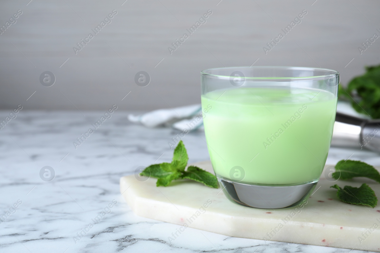 Photo of Delicious mint liqueur with ice cubes and green leaves on white marble table, closeup. Space for text