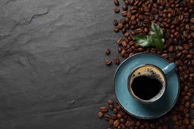 Photo of Cup of aromatic hot coffee and beans on black table, flat lay. Space for text