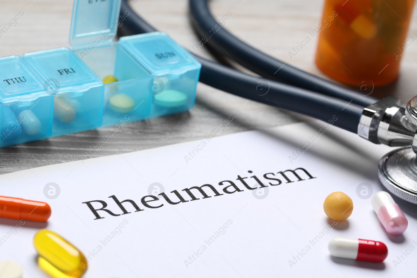 Photo of Paper with word Rheumatism, stethoscope and pills on table, closeup