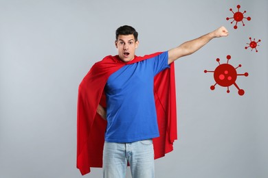 Man wearing superhero costume ready to fight against viruses on light grey background
