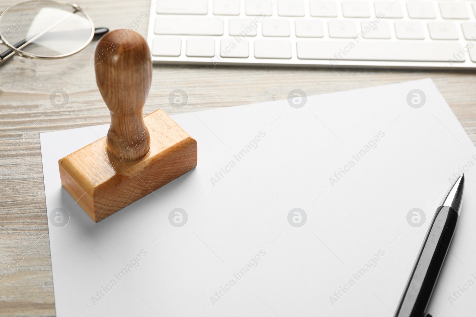 Photo of Blank sheet of paper, pen, glasses, keyboard and stamp on wooden table