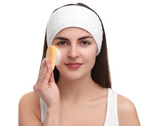 Photo of Young woman with headband washing her face using sponge on white background