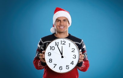 Photo of Man in Santa hat with clock on blue background. Christmas countdown
