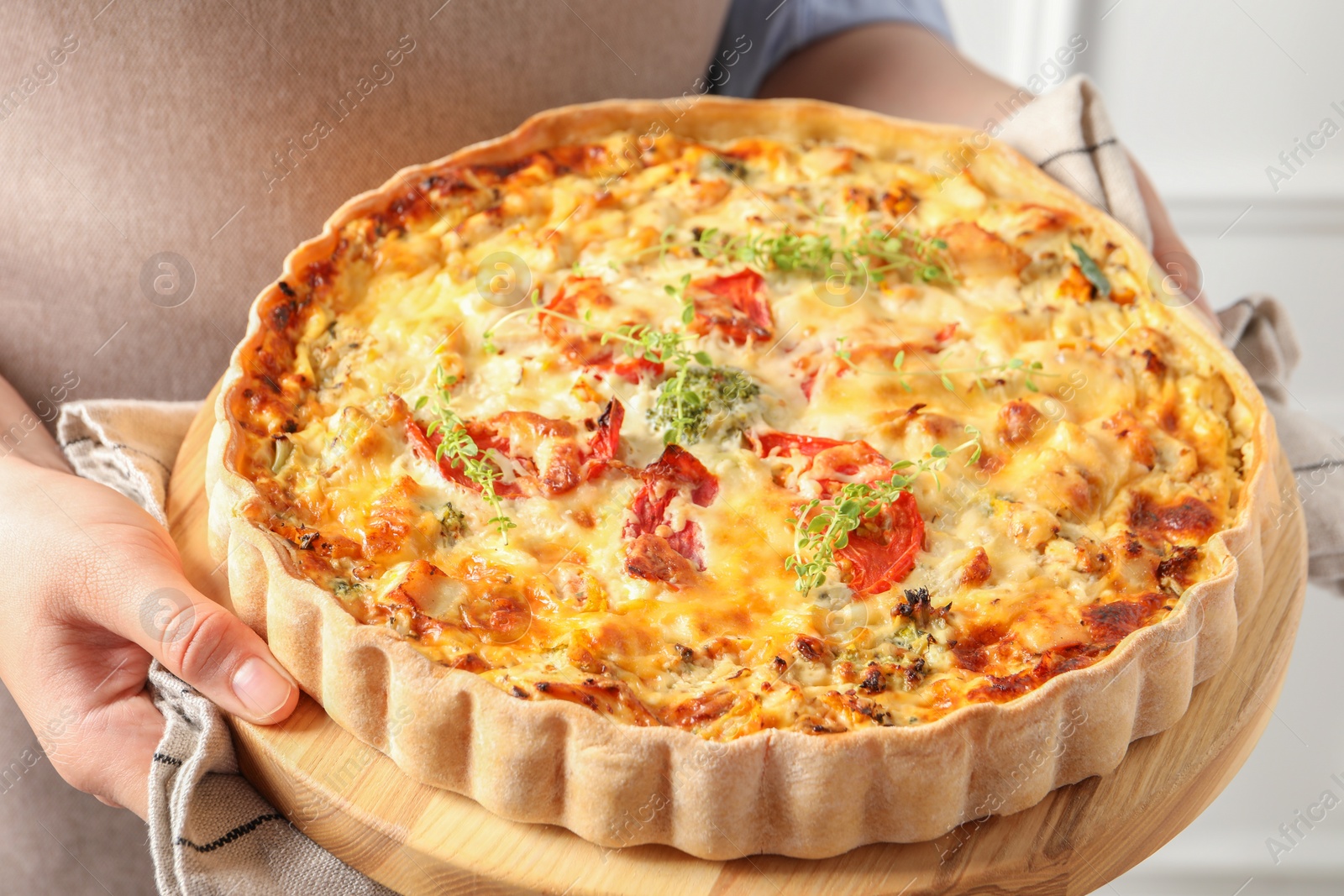 Photo of Woman holding board with tasty quiche indoors, closeup