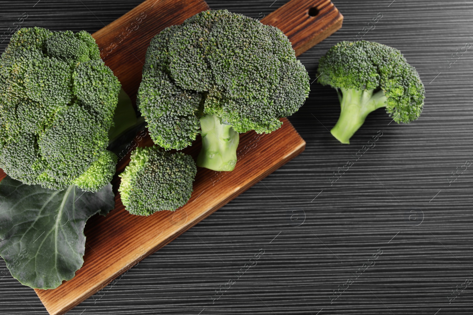 Photo of Board with fresh raw broccoli on black wooden table, above view. Space for text