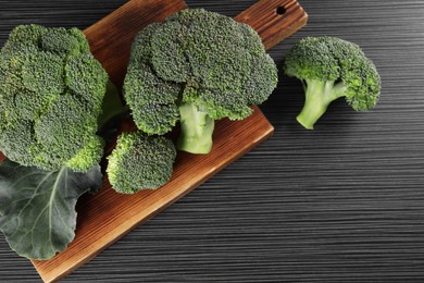 Photo of Board with fresh raw broccoli on black wooden table, above view. Space for text