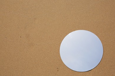 Photo of Round mirror reflecting sky on sand outdoors, top view. Space for text