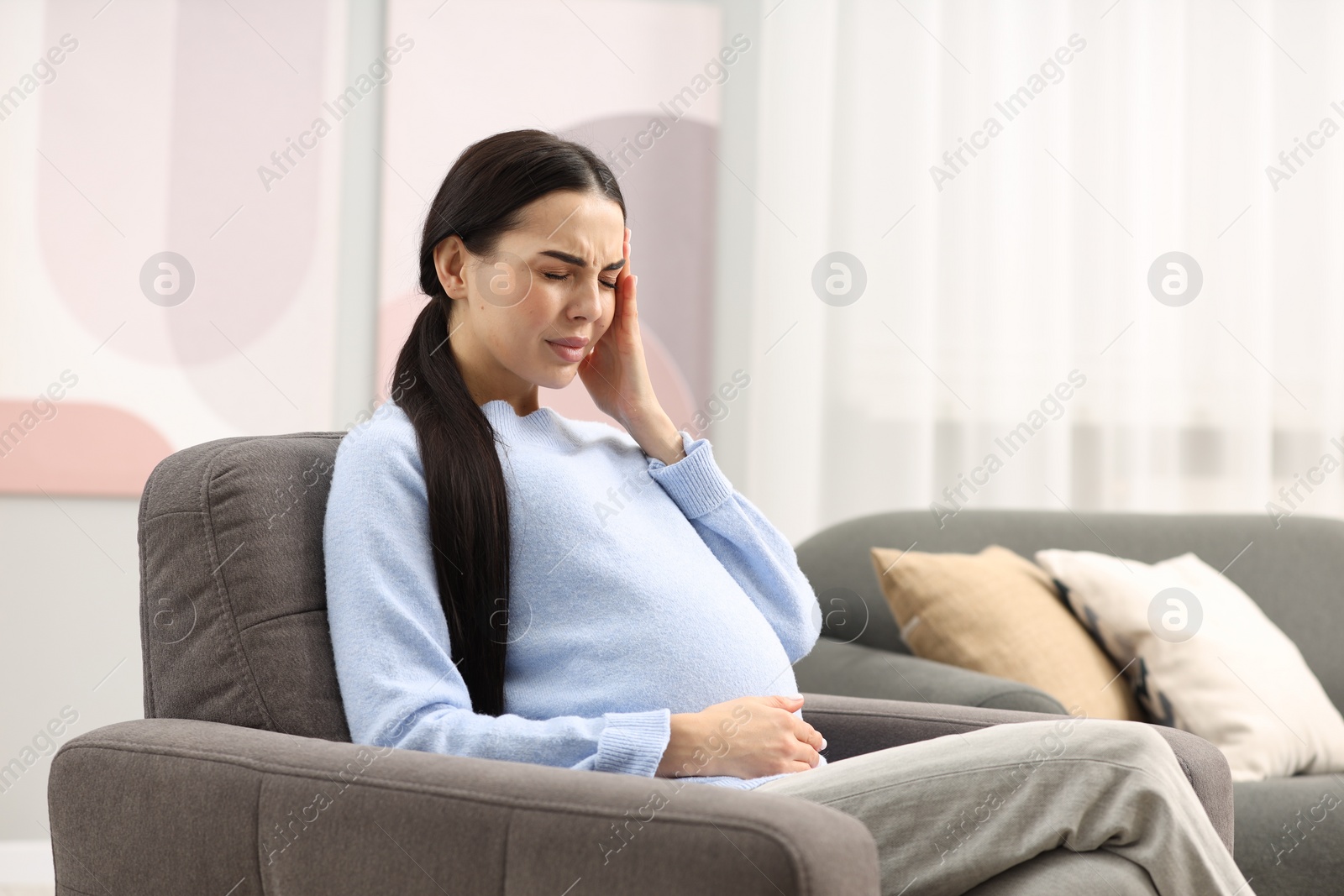 Photo of Pregnant woman suffering from headache on armchair at home