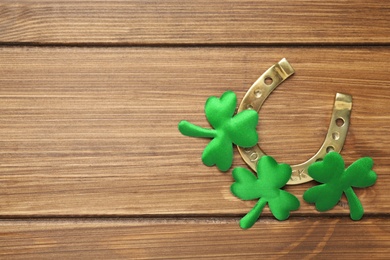 Decorative clover leaves and horseshoe on wooden background, flat lay with space for text. St. Patrick's Day celebration