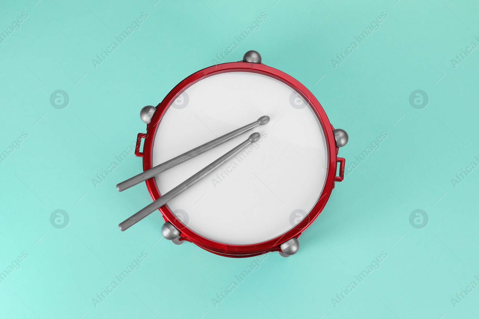 Photo of Children's drum with drumsticks on turquoise background, top view
