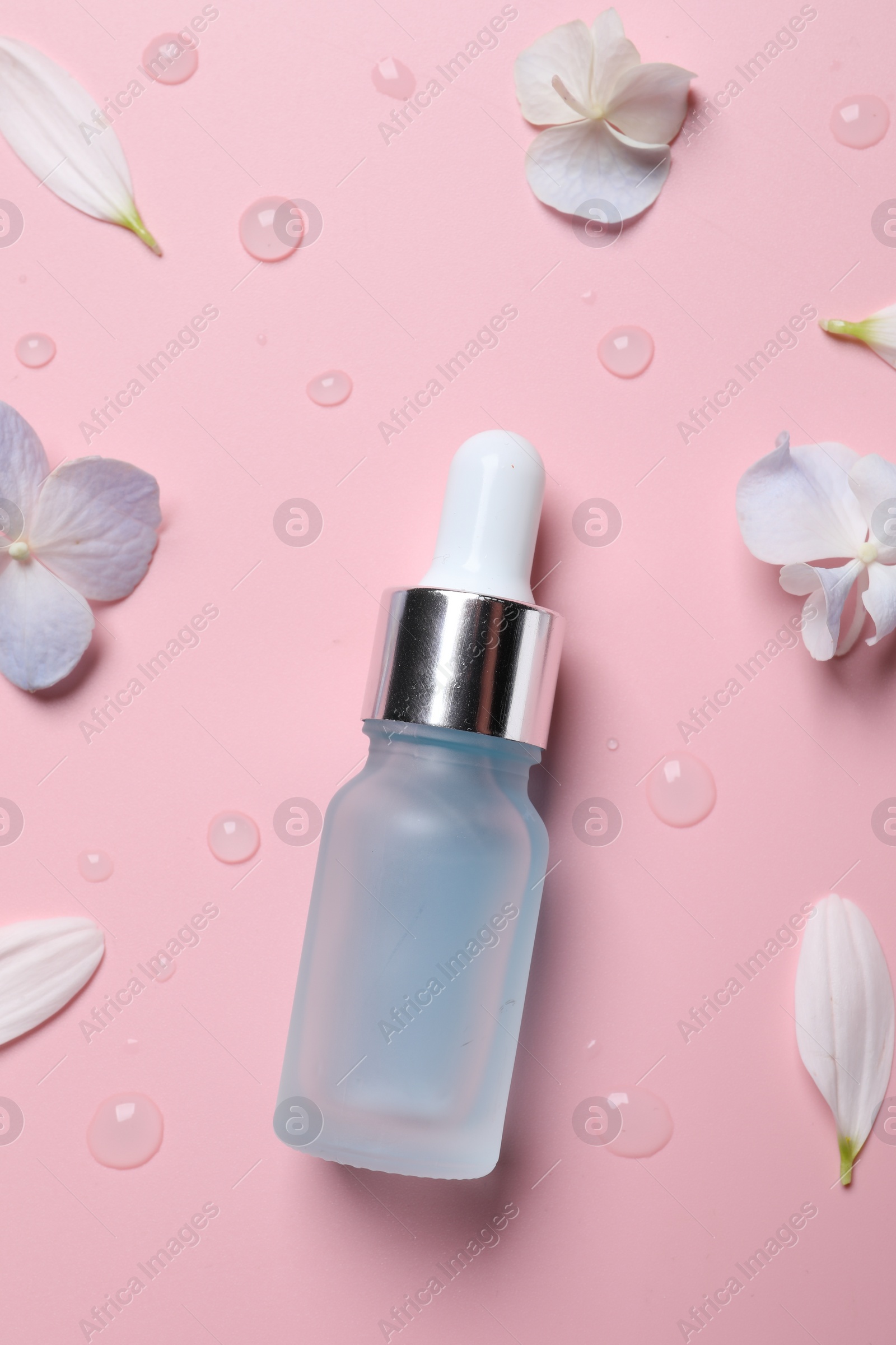 Photo of Bottle of cosmetic serum and beautiful flowers on pink background, flat lay