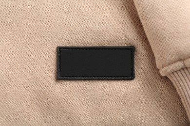 Photo of Blank clothing label on beige sweatshirt, top view