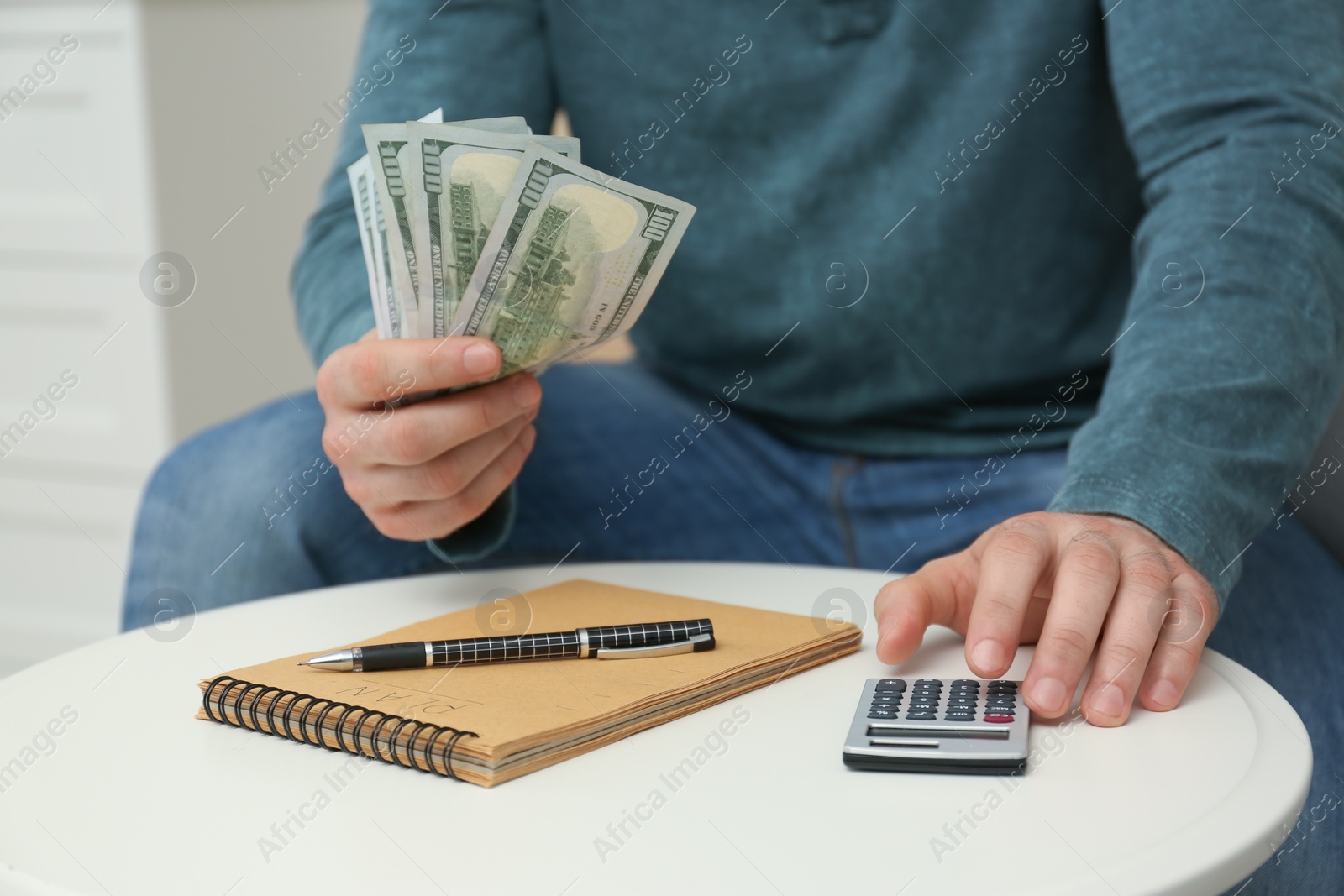 Photo of Man with money, notebook and calculator at table indoors, closeup