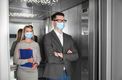 Photo of Coworkers with face masks in elevator. Protective measure