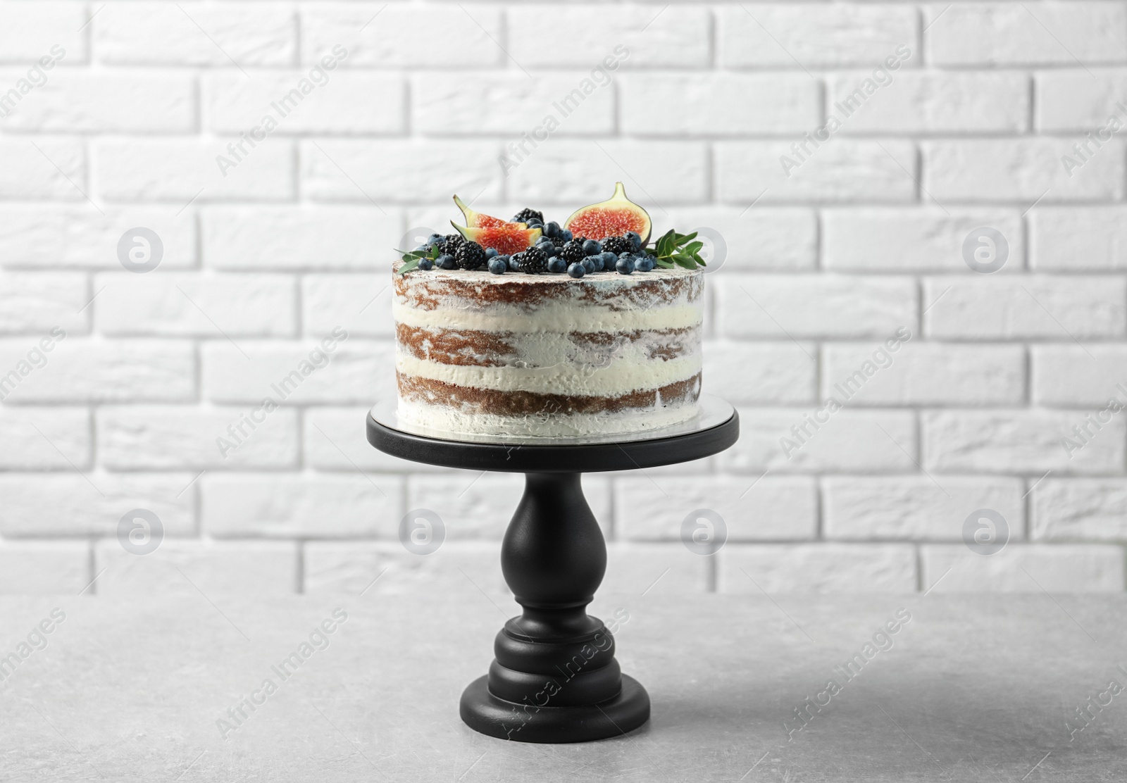 Photo of Delicious homemade cake with fresh berries on table near brick wall