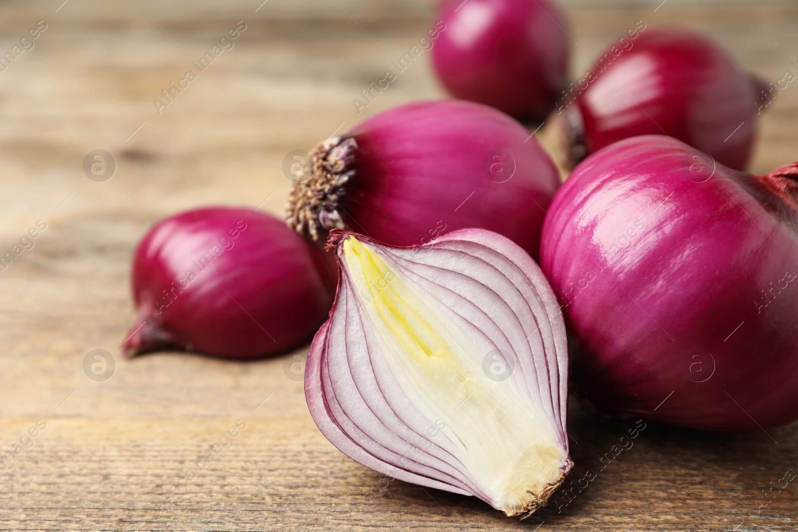 Photo of Ripe red onion bulbs on wooden table, closeup