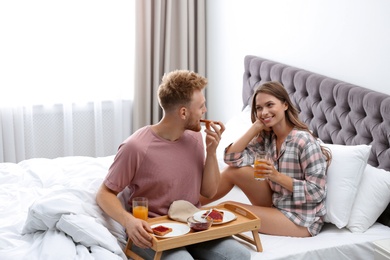 Photo of Happy young couple having romantic breakfast on bed at home