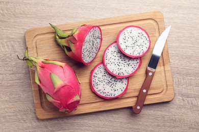 Photo of Board with delicious white pitahaya fruits and knife on wooden table, top view