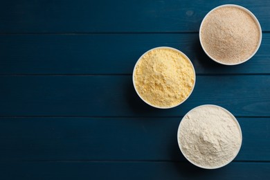 Photo of Different types of flours in bowls on blue wooden table, flat lay. Space for text