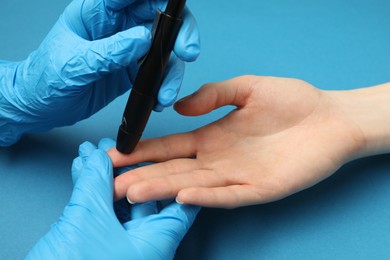 Diabetes. glucose testing. Doctor using lancet pen on blue background, closeup