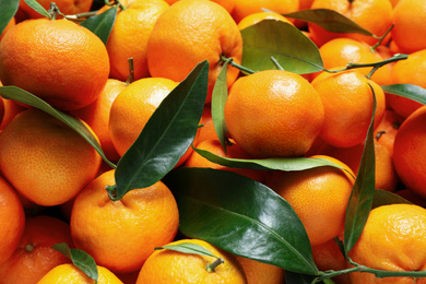Photo of Fresh ripe tangerines with leaves as background, closeup. Citrus fruit