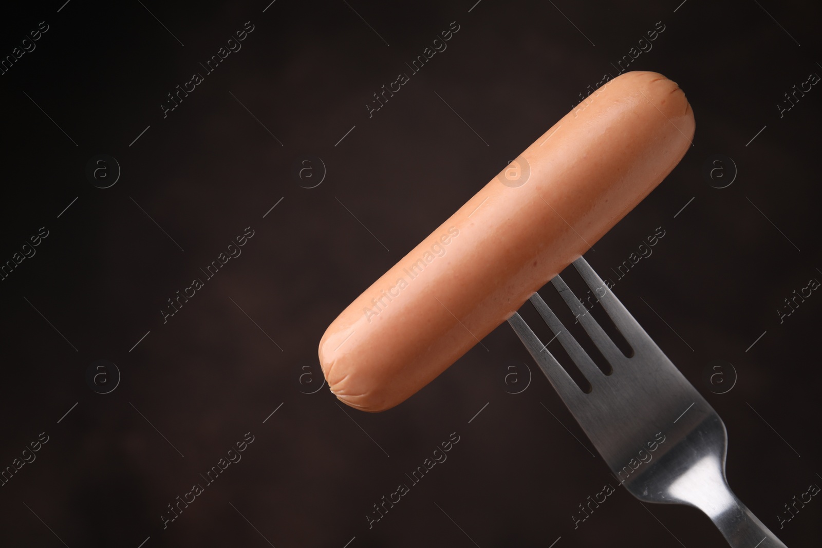 Photo of Delicious boiled sausage on fork against dark background, closeup. Space for text